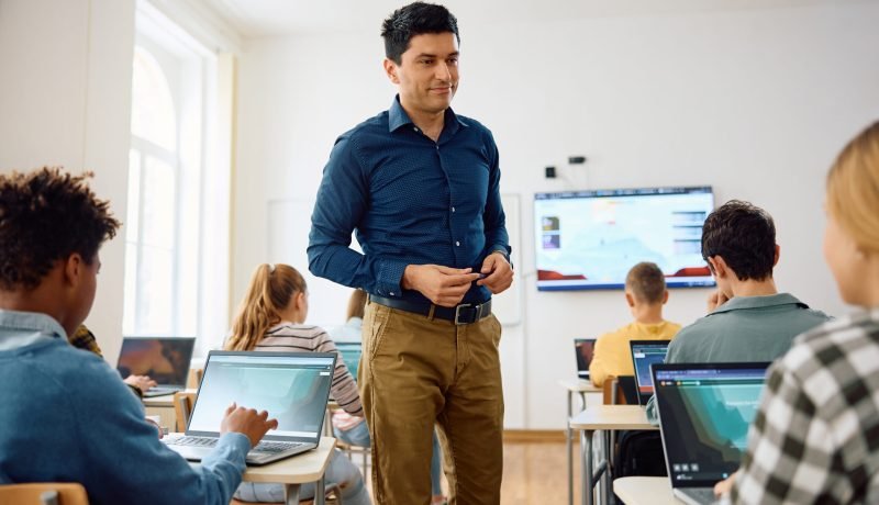 Happy computer science professor teaching students during a class in the classroom.